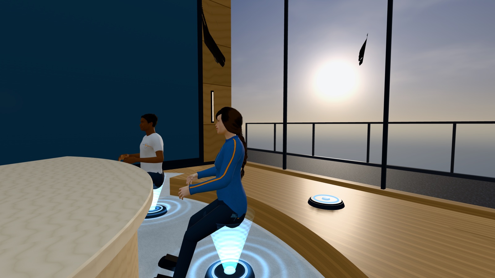 Two colleagues seated at the table in front of floor-to-ceiling windows with the sun low over the sea